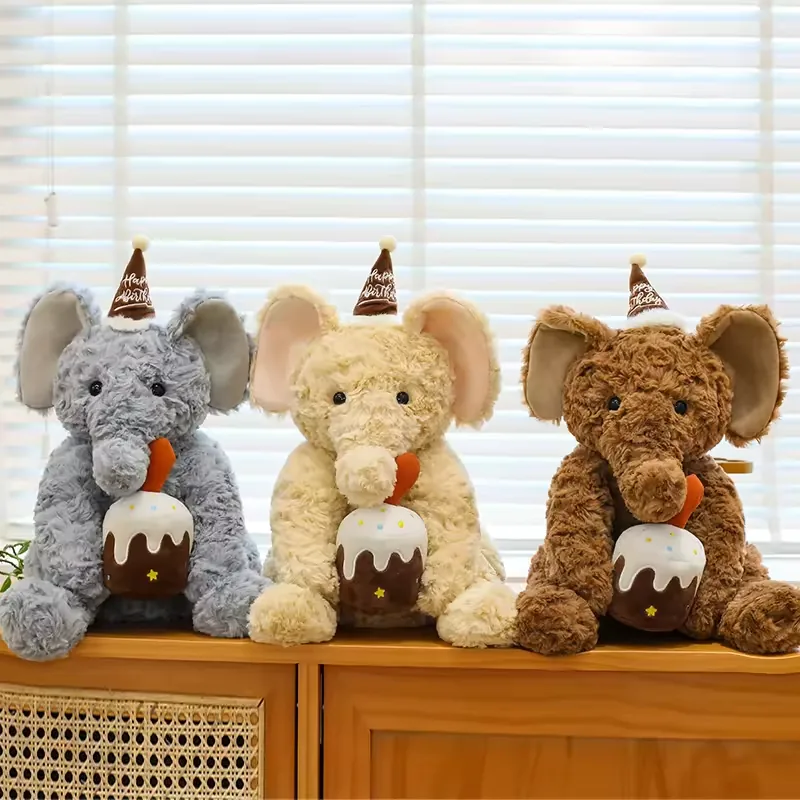 Three birthday elephant plush dolls in grey, cream, and brown seated together with cake accessories and party hats