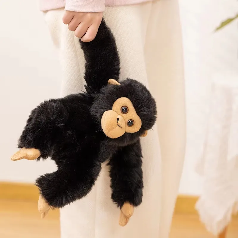 Black chimpanzee plush doll held by one arm to show flexible body and carry-friendly size