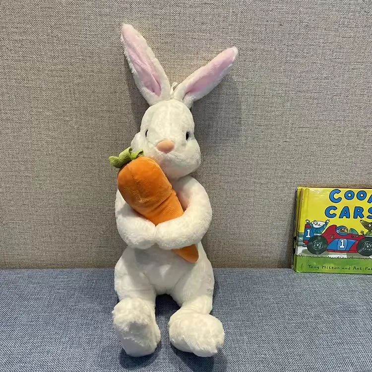 White rabbit plush doll with pink inner ears hugging an oversized carrot