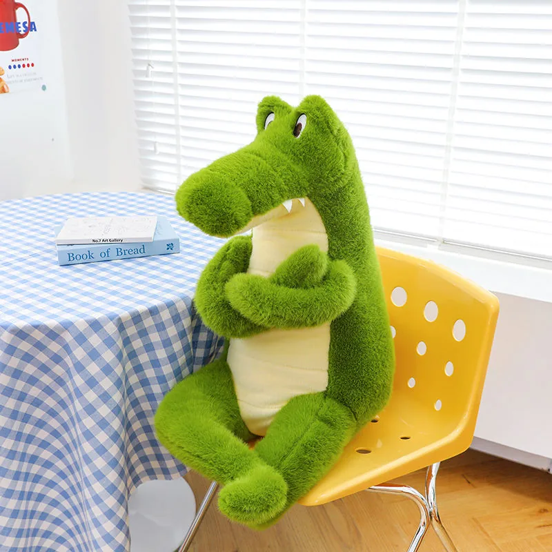 Single green crocodile plush doll sitting upright beside a table with crossed arms and a long snout