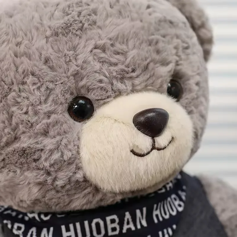 Close-up of grey teddy bear plush face with cream muzzle, dark nose, and glossy black eyes