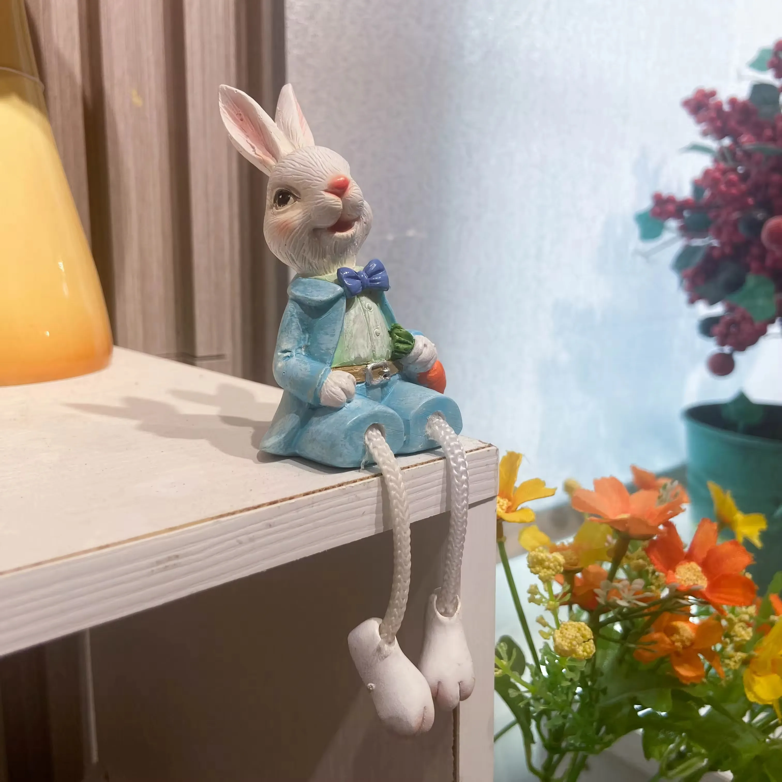Hand-painted resin rabbit shelf sitter in a blue jacket with dangling rope legs and a carrot accent