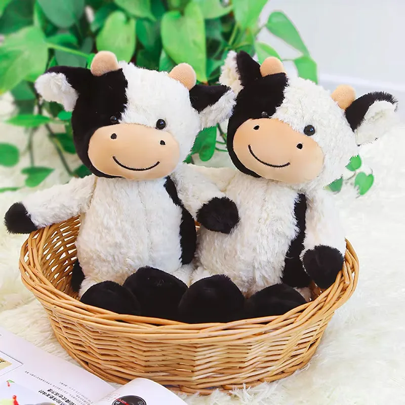 Two milk cow plush dolls sitting together in a wicker basket with black-and-white patch fur and soft peach muzzles