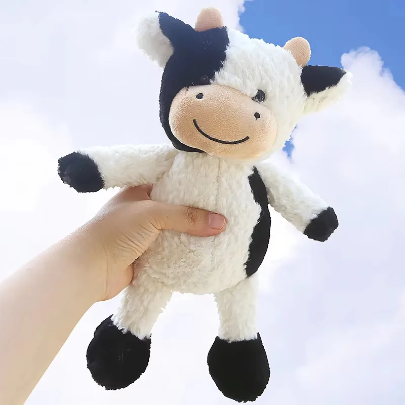 Hand holding a milk cow plush doll to show soft body size, floppy limbs, and black hoof details