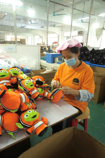 Factory worker hand-stuffing small orange plush toys at a production table