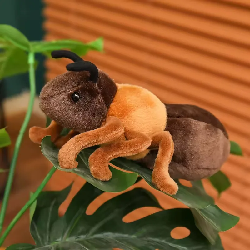 Realistic ant plush toy resting on a large green leaf with visible segmented body and curved antennae