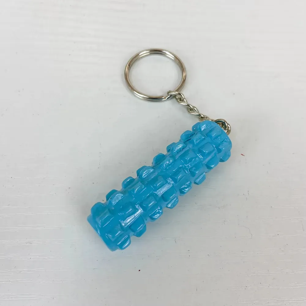 Angled view of a blue foam roller resin keychain with cylindrical textured pattern