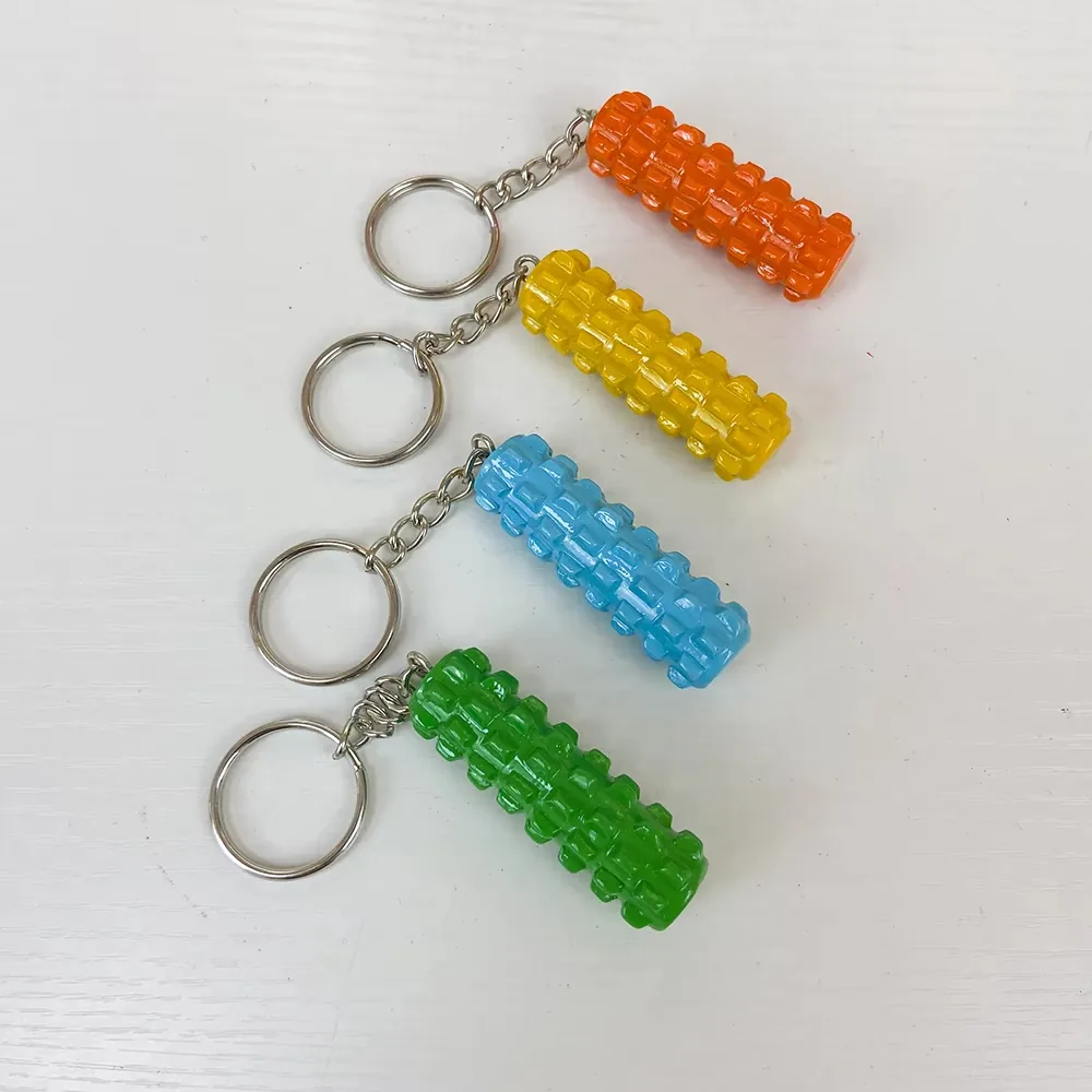 Four foam roller resin fitness keychains in orange, yellow, blue, and green arranged as a textured gym accessory collection