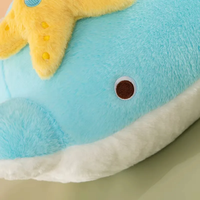 Close-up of the blue dolphin plush pillow face with round embroidered eye and white belly edge