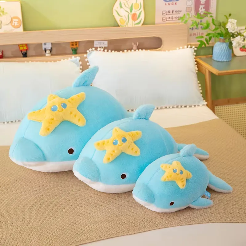 Three blue dolphin plush pillows shown together in small, medium, and large sizes on a bed