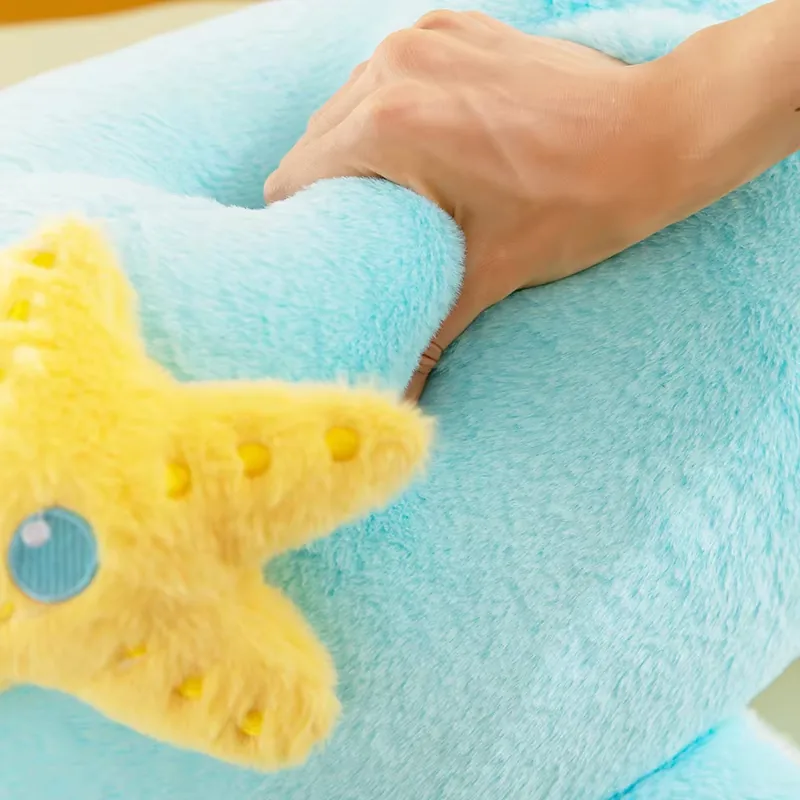 Hand pressing the blue dolphin plush pillow to show soft surface texture and resilience