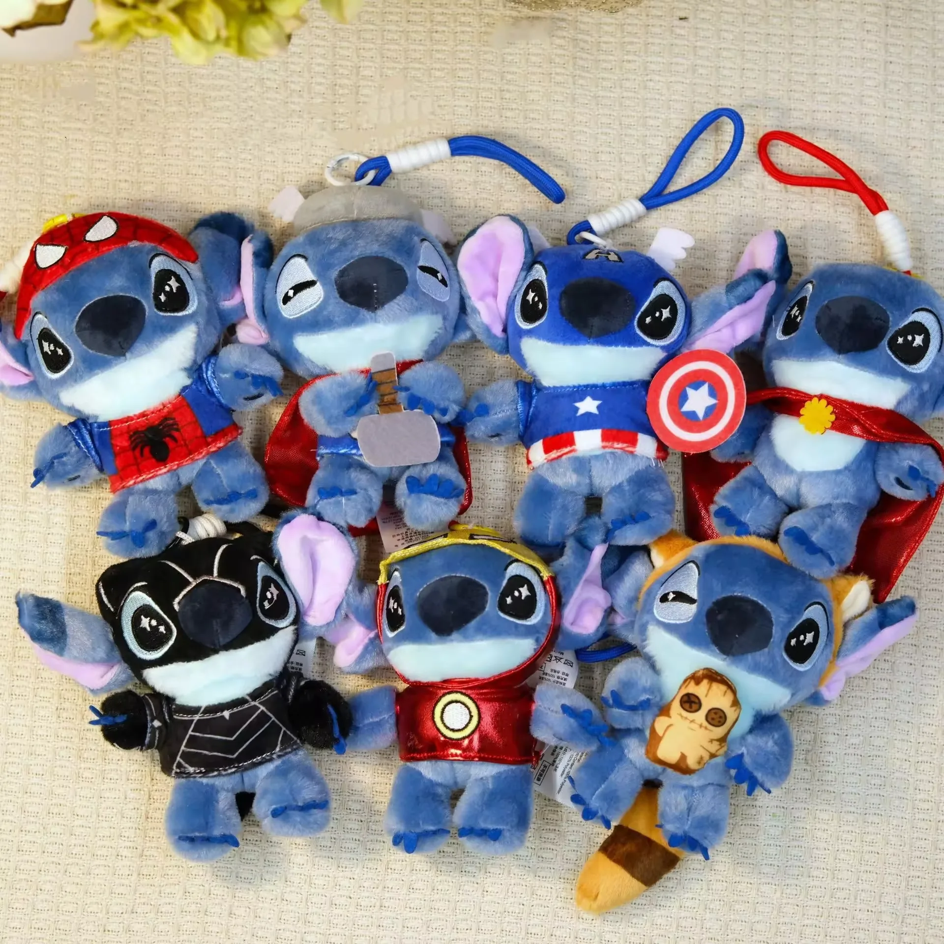 A lineup of Stitch superhero keychain plush charms shown in multiple costume variants with hanging loops