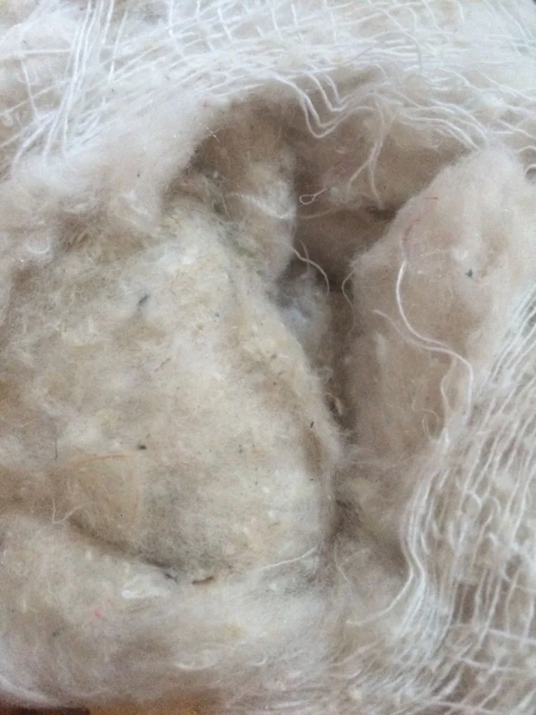 Close-up of low-grade plush filling with gray tones, dense clumps, and visible contamination