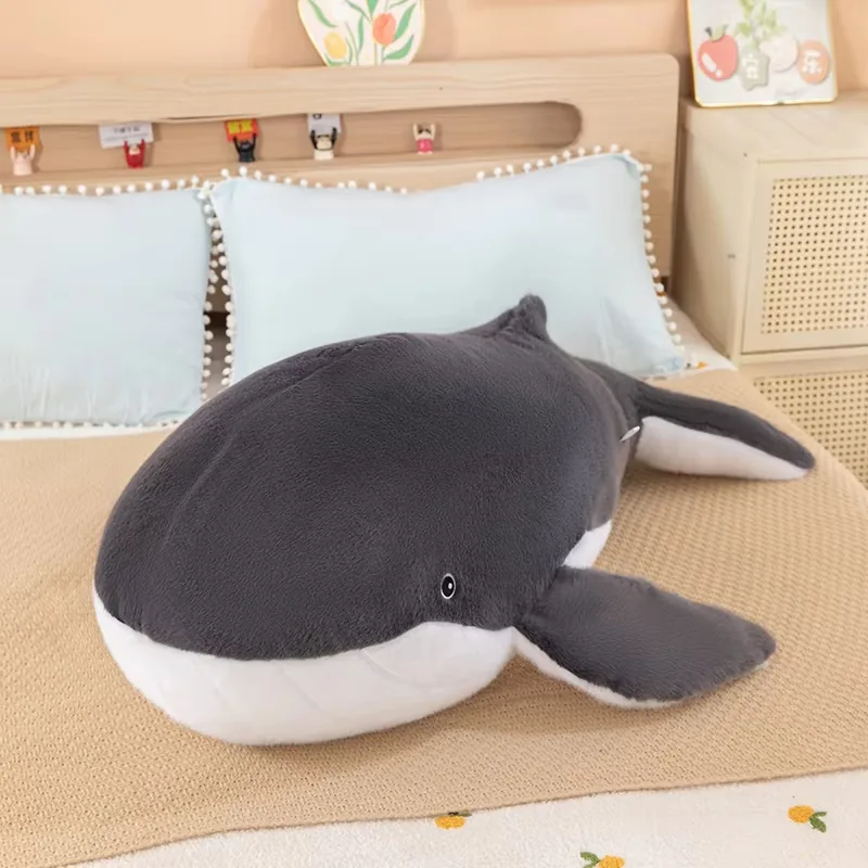 Single whale plush pillow displayed on a bed with a rounded body, white belly, and long tail