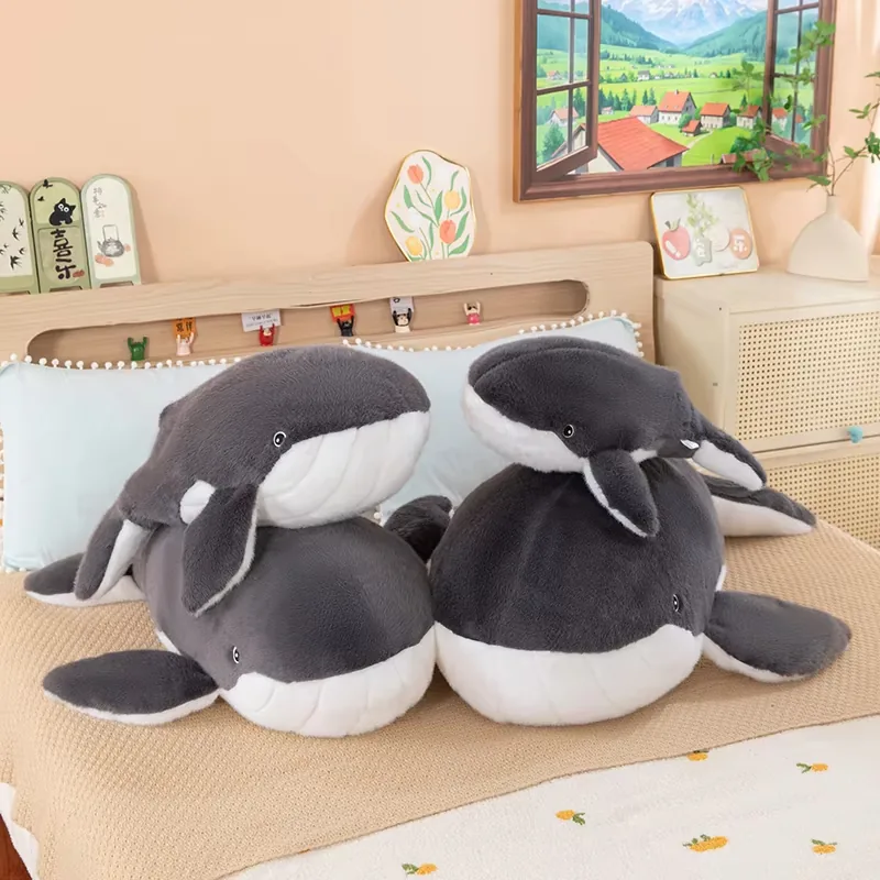Three grey-and-white whale plush pillows grouped together on a bed as a soft ocean-animal collection