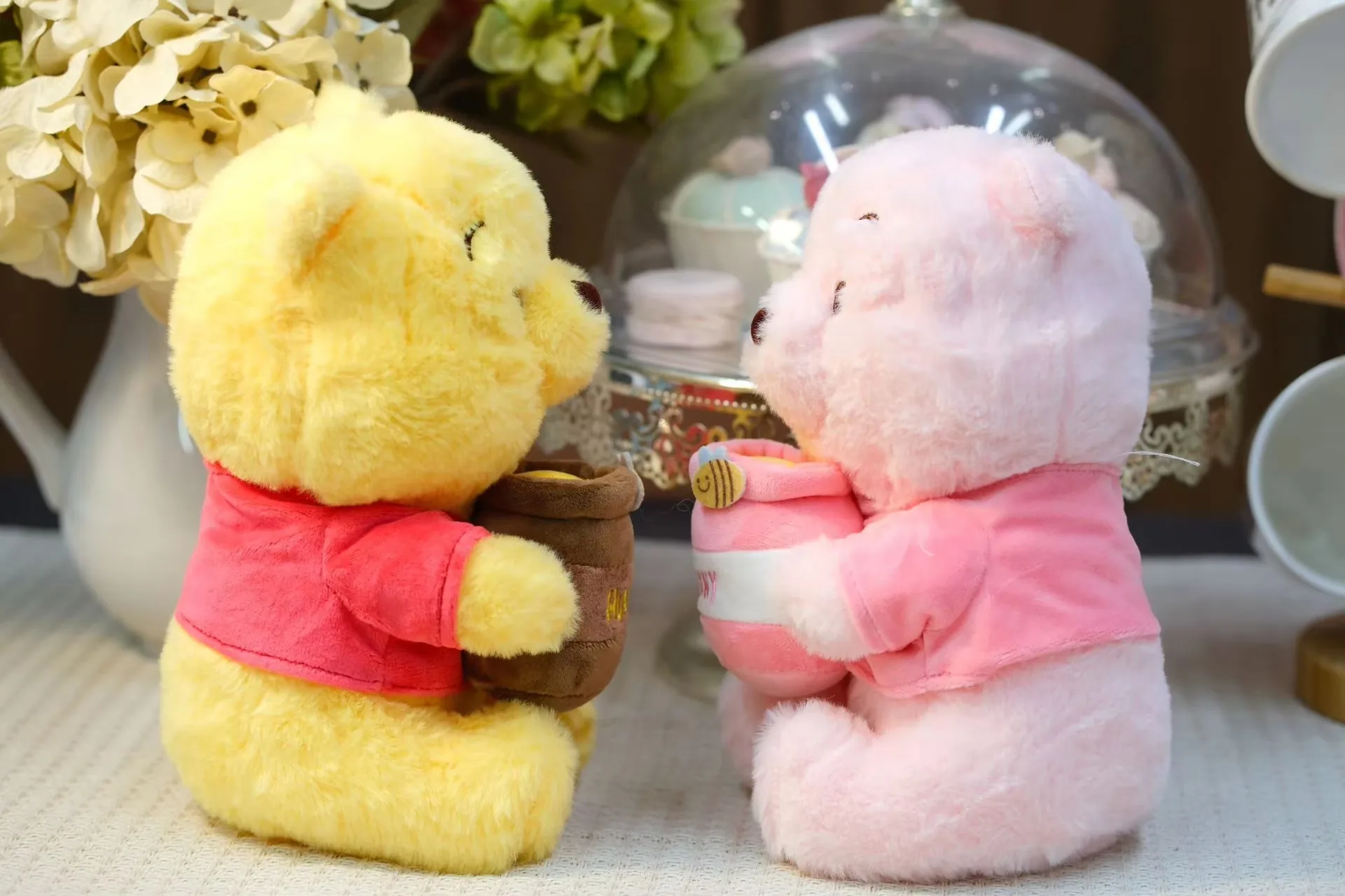 Side view of the yellow and pink honey jar bear plush dolls sitting face to face